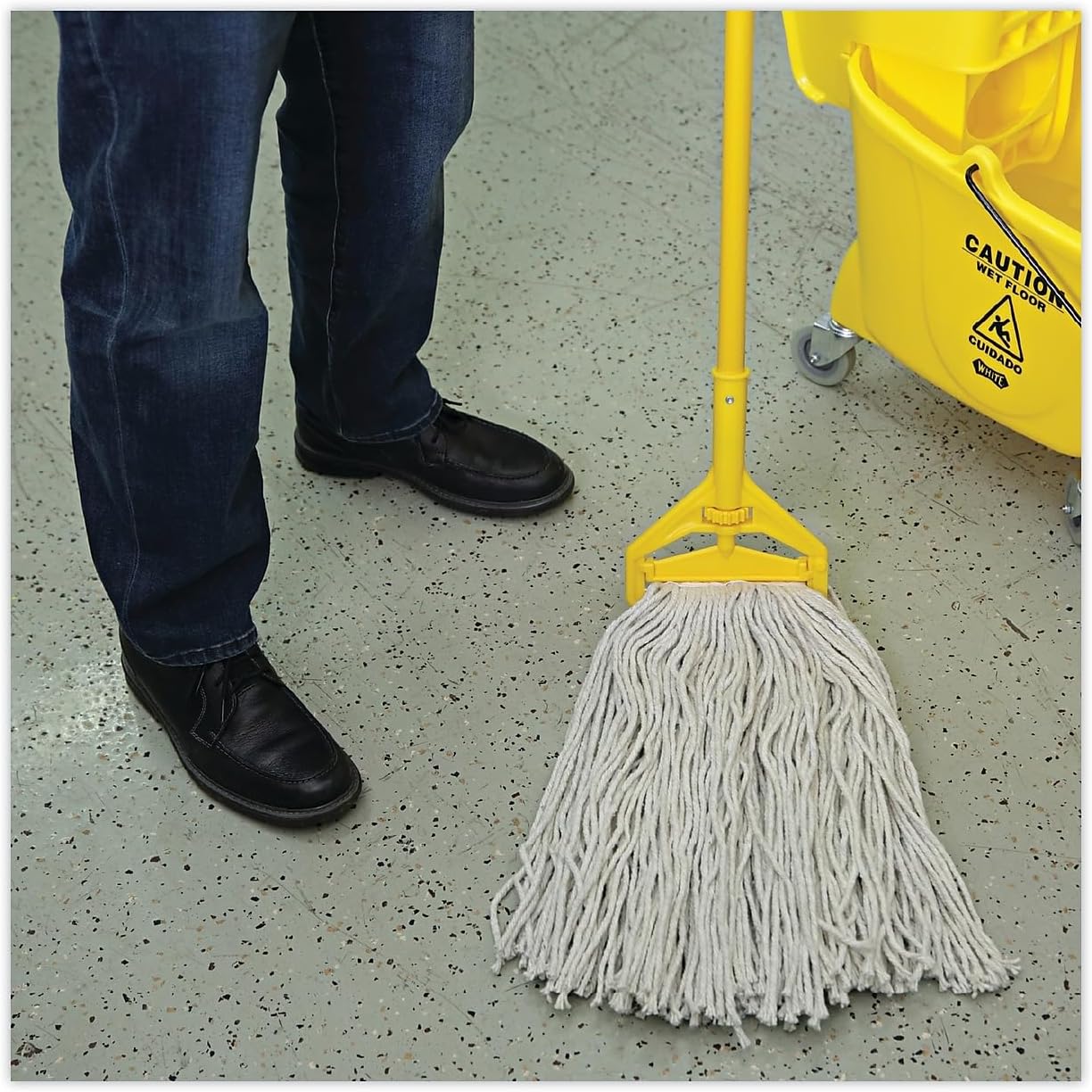 Mop with a yellow handle on a concrete floor next to a yellow mop bucket.